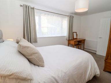 A bedroom with a bed a wooden dressing table with a mirror and a large window at 3 Granbrook Lane in Mickleton Gloucestershire