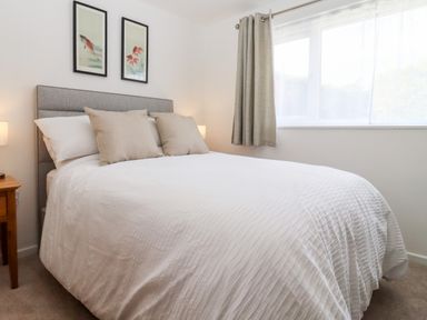 A bedroom with a bed with white bedding and two beige pillows by a window with curtains at 3 Granbrook Lane in Mickleton Gloucestershire