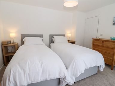 A bedroom with two single beds bedside tables with lamps a wooden dresser and a closed door at 3 Granbrook Lane Mickleton Gloucestershire
