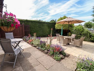 A garden patio with two seating areas surrounded by flower beds and green hedges at 3 Granbrook Lane in Mickleton Gloucestershire