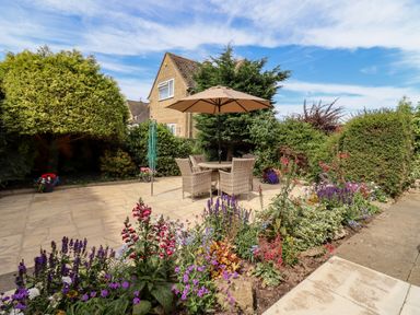 A garden patio with table umbrella chairs and flower beds at 3 Granbrook Lane in Mickleton Gloucestershire
