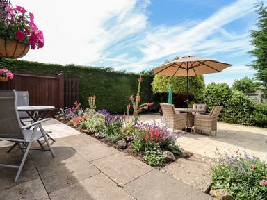 A garden patio with outdoor tables chairs an umbrella and flowerbeds at 3 Granbrook Lane Mickleton Gloucestershire