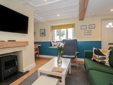 A living room with a green sofa a gray armchair a white coffee table with flowers and a fireplace at Holly Cottage in West Coker