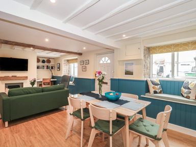 A living and dining area with a green sofa a wooden dining table with chairs and a window bench seat at Holly Cottage in West Coker
