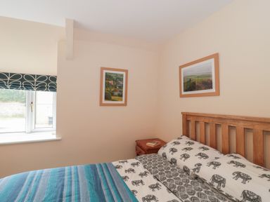 A bedroom with a wooden bed frame striped bedding and elephant patterned pillows with framed pictures on the wall at Holly Cottage in West Coker