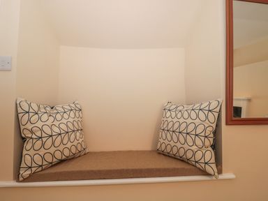 A small window seat with two patterned cushions and a brown seat pad at Holly Cottage in West Coker