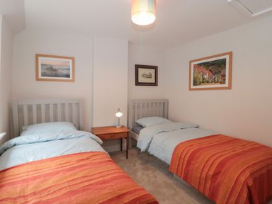 A bedroom with two single beds with orange striped blankets and a wooden nightstand with a lamp between them at Holly Cottage in West Coker