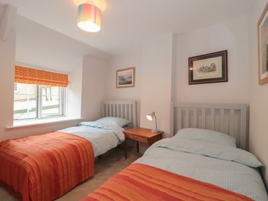 A bedroom with two single beds a wooden bedside table and a window with an orange blind at Holly Cottage in West Coker