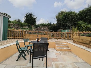 An outdoor patio with a table and four chairs with a bottle and two glasses on the table at Holly Cottage in West Coker