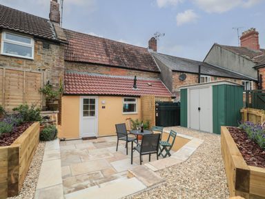 A backyard patio with a small table and chairs outside a yellow house with a tiled roof at Holly Cottage in West Coker