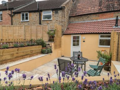 A small outdoor patio with a round table and chairs next to a yellow building with a tiled roof at Holly Cottage in West Coker