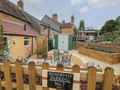 A fenced garden area with a patio table and chairs and a sign for reserved parking at Holly Cottage in West Coker