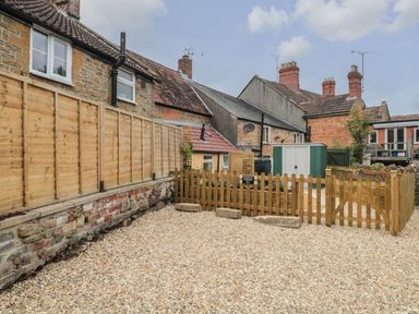 A gravel area with wooden fencing and stone walls near residential buildings at Holly Cottage in West Coker