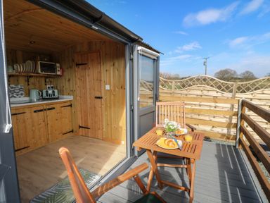 A small wooden kitchen inside with a countertop and appliances next to a wooden deck with a table set for breakfast at Claerwen Nant-glas near Rhayader