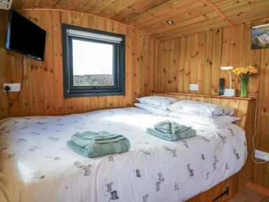 A bedroom with a bed covered in white bedding with patterns with two folded towels on it and wooden walls at Claerwen in Nant-glas near Rhayader