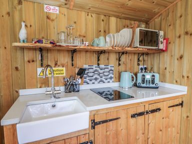 A small kitchen area with a sink stove microwave kettle and toaster at Claerwen in Nant-glas near Rhayader