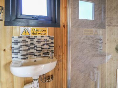 A small sink with a faucet and tiled backsplash under a window with a caution hot water sign at Claerwen in Nant-glas near Rhayader