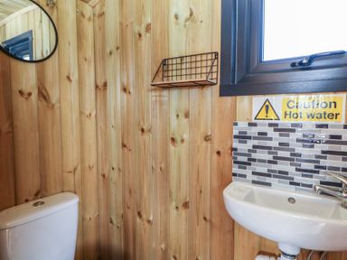 A bathroom with wooden walls a toilet a round mirror a small sink and a caution hot water sign at Claerwen Nant-glas near Rhayader