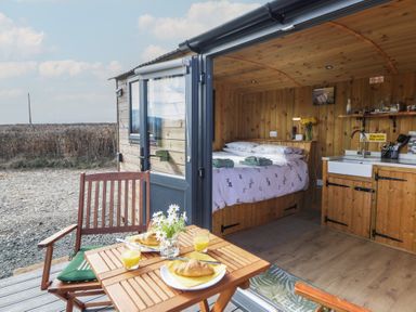 A small wooden cabin interior with a bed and kitchenette and an outdoor wooden table with chairs and breakfast at Claerwen in Nant-glas near Rhayader