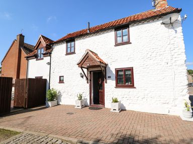 A white stone house with red roof tiles and brown window frames with a paved driveway at Chalk Cottage in Feltwell