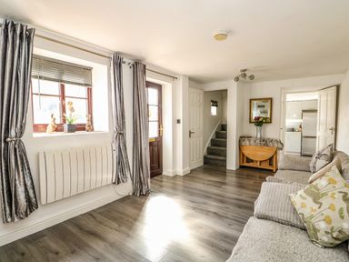 A living room with a sofa a wooden door stairs and a table with a vase of flowers at Chalk Cottage in Feltwell