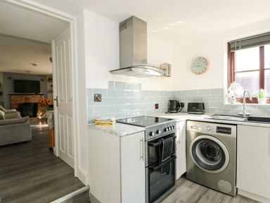 A kitchen with a stove washing machine toaster kettle and window looking into a living room at Chalk Cottage in Feltwell