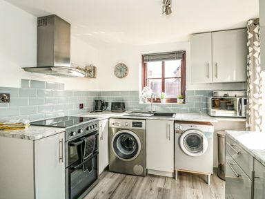 A kitchen with a stove washing machine dryer microwave and window at Chalk Cottage in Feltwell