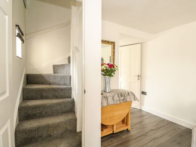 A staircase with grey carpet and a small breakfast table with a floral vase in a room with wood flooring at Chalk Cottage in Feltwell