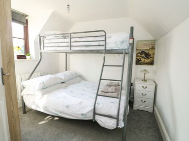A bedroom with metal bunk beds next to a window a bedside table with a lamp and a painting on the wall at Chalk Cottage in Feltwell
