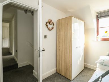 A corner of a bedroom with a wardrobe a bed and a window showing a hallway at Chalk Cottage in Feltwell