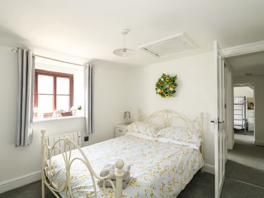 A bedroom with a bed covered in floral bedding a window with curtains and a wreath on the wall at Chalk Cottage in Feltwell
