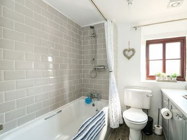 A bathroom with a bathtub shower combination toilet window and vanity at Chalk Cottage in Feltwell