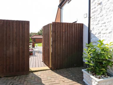 A wooden gate opening to a decked patio with outdoor furniture and plants at Chalk Cottage in Feltwell