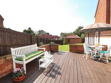 An outdoor patio with a white bench and a table with an umbrella and chairs at Chalk Cottage in Feltwell