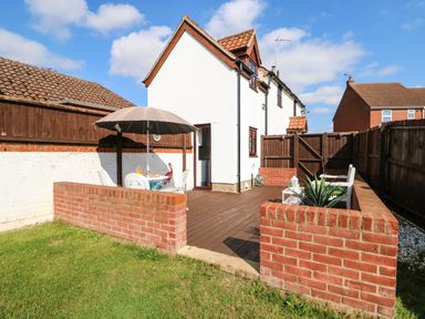An outdoor patio area with a table and umbrella chairs enclosed by low brick walls at Chalk Cottage in Feltwell