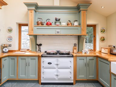 A kitchen with green cabinets wooden countertops white stove with kettles and utensils at Eagle Farmhouse in Glenridding