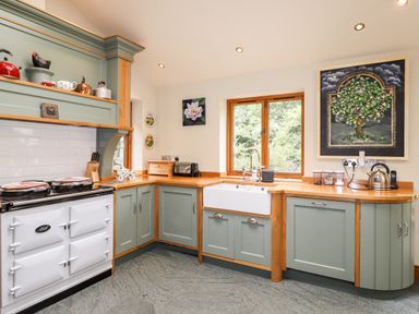 A kitchen with green cabinets wooden countertops a white stove a window above a white sink and artwork on the walls at Eagle Farmhouse in Glenridding
