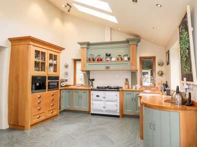 A kitchen with green and wood cabinets a white stove skylights and various kitchen items on counters and shelves at Eagle Farmhouse in Glenridding