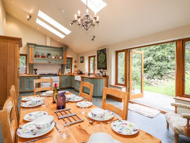 A kitchen with green cabinets a wooden dining table set with plates and bowls and an open door leading to a garden at Eagle Farmhouse in Glenridding