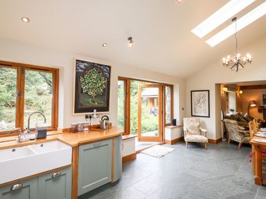 A kitchen with a white sink wooden countertops green cabinets and wooden framed windows at Eagle Farmhouse in Glenridding