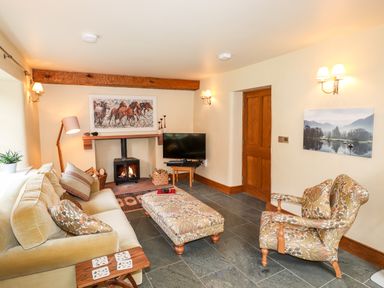A living room with a sofa a patterned armchair a fireplace and a television at Eagle Farmhouse in Glenridding