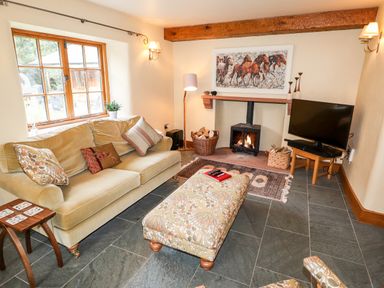 A living room with a sofa and ottoman near a fireplace with a wood stove and a television at Eagle Farmhouse in Glenridding