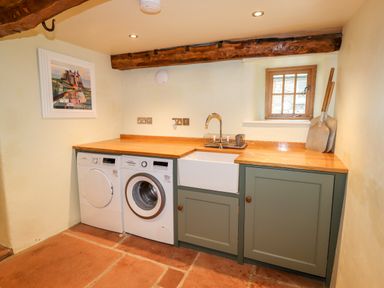 A laundry room with washing machine dryer sink wooden countertop wooden cabinets and small window at Eagle Farmhouse in Glenridding