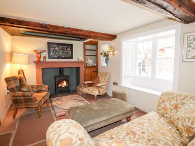 A sitting room with a fireplace armchairs a window seat and a cushioned ottoman at Eagle Farmhouse in Glenridding