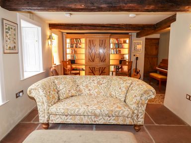 A living room with a floral sofa in front of a wooden bookshelf with books and two wooden chairs at Eagle Farmhouse in Glenridding