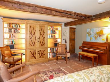 A room with wooden bookcases, chairs, a piano, guitar, and a world map on the wall at Eagle Farmhouse in Glenridding