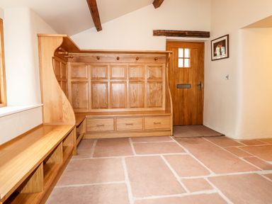 An entryway with wooden bench seating hooks and drawers a wooden door and tiled floor at Eagle Farmhouse in Glenridding