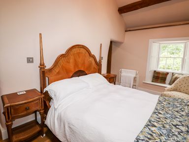 A bedroom with a wooden bed and nightstands next to a window with cushions at Eagle Farmhouse in Glenridding