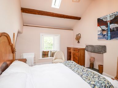 A bedroom with a bed a wooden dresser an upholstered chair and a window with cushions at Eagle Farmhouse in Glenridding