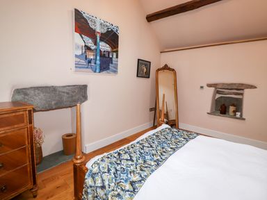 A bedroom with a wooden bed white bedding a chest of drawers a standing mirror and two stone wall niches at Eagle Farmhouse in Glenridding
